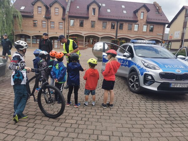 Na zjęciu policjant wręczający opaski odblaskowe dzieciom uczestniczącym w rajdzie rowerowym